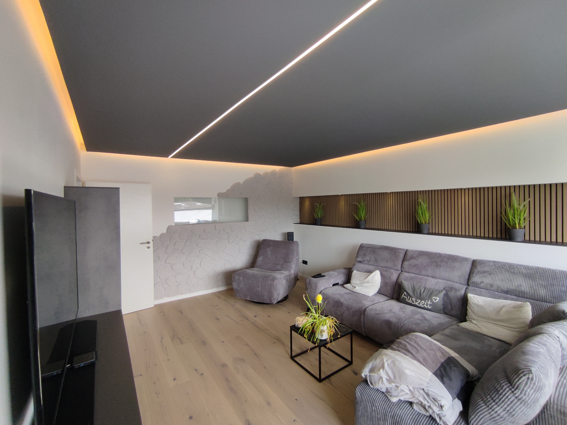 Wohnzimmer mit abgehängter Decke, LED-Lichtband und Akustik-Holzpaneelen