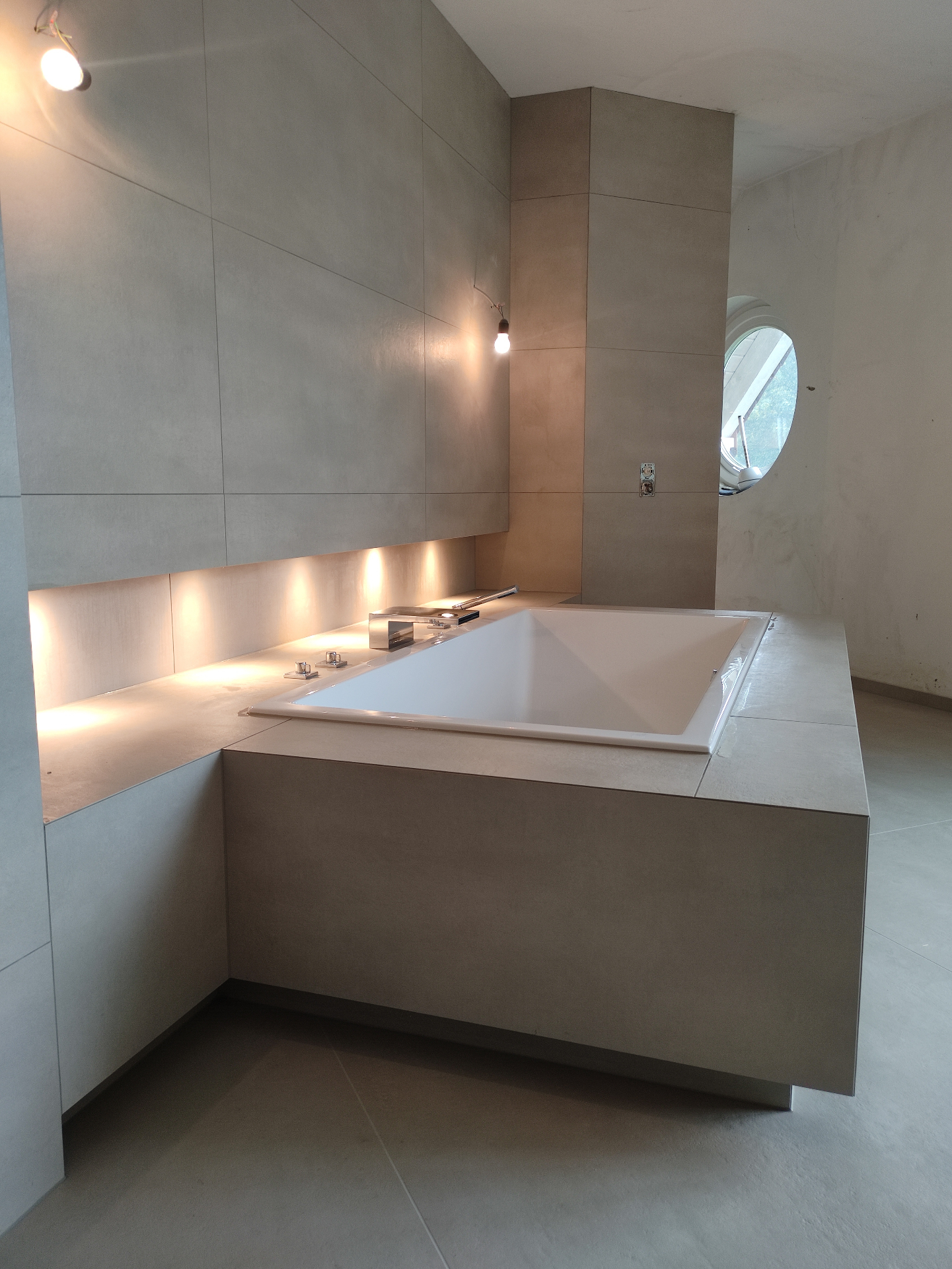 Eingelassene Badewanne mit großformatigen Wandfliesen und indirekter Beleuchtung